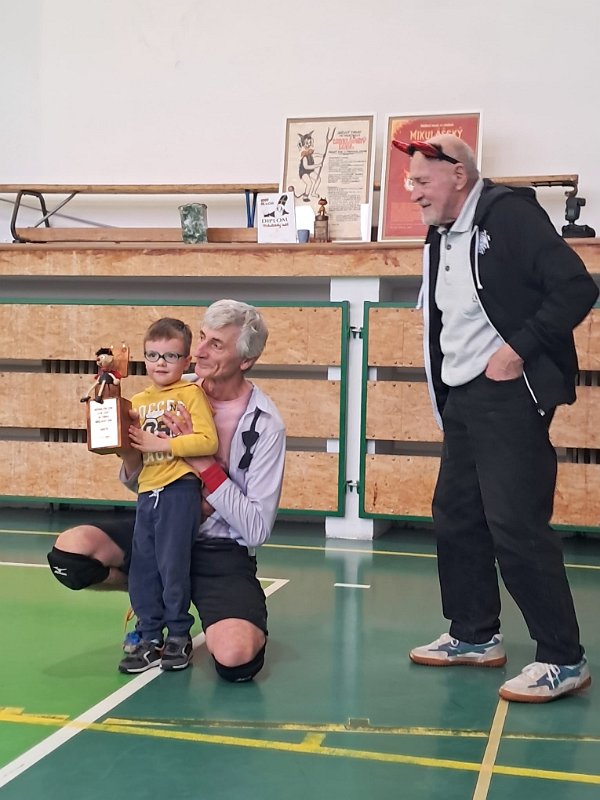 IMG-20251206-WA0005.jpg - Dostal jsem Buchholzovu cenu za celoživotní zásluhy o Mikulášský debl. Cenu vymysleli Michal s Borisem, předává ji Toník s Ádou. Jsem natolik dojat, že půl dalšího setu nevidím na míč.